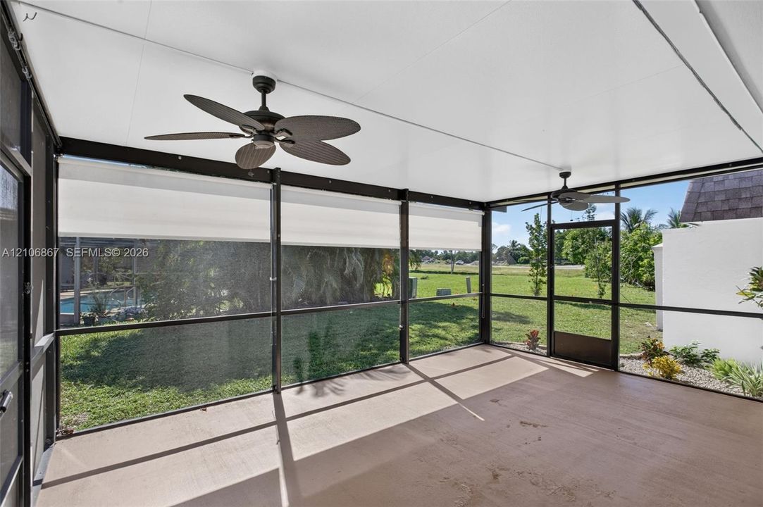 Screened-in lanai featuring a solid roof, ceiling fans, concrete flooring, and metal framing