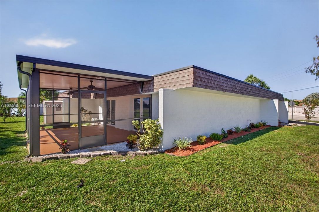 Screened-in rear porch featuring built-in ceiling fans, textured masonry exterior, shingled roofline, and landscaped rock garden beds