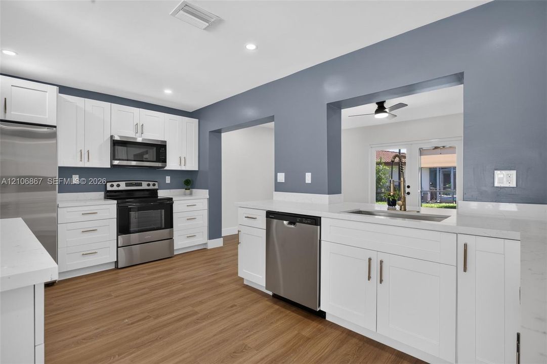 Kitchen featuring white Shaker-style cabinetry, stainless steel appliances, quartz countertops, wood-finish flooring, and recessed lighting