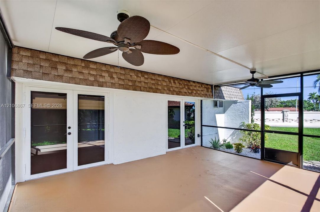 Screened-in patio featuring concrete flooring, dual ceiling fans, shingle-accented wall cladding, and multiple glass-paned double doors