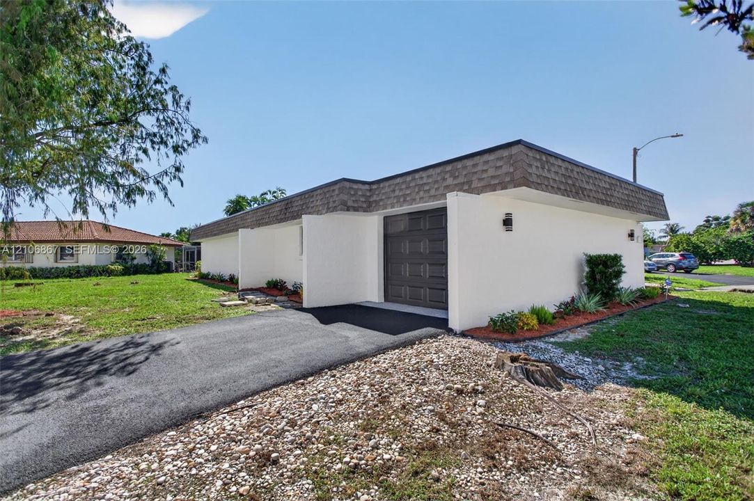 Single-story exterior featuring white stucco siding, a flat roofline with shingle-style trim, an attached one-car garage, and an asphalt driveway