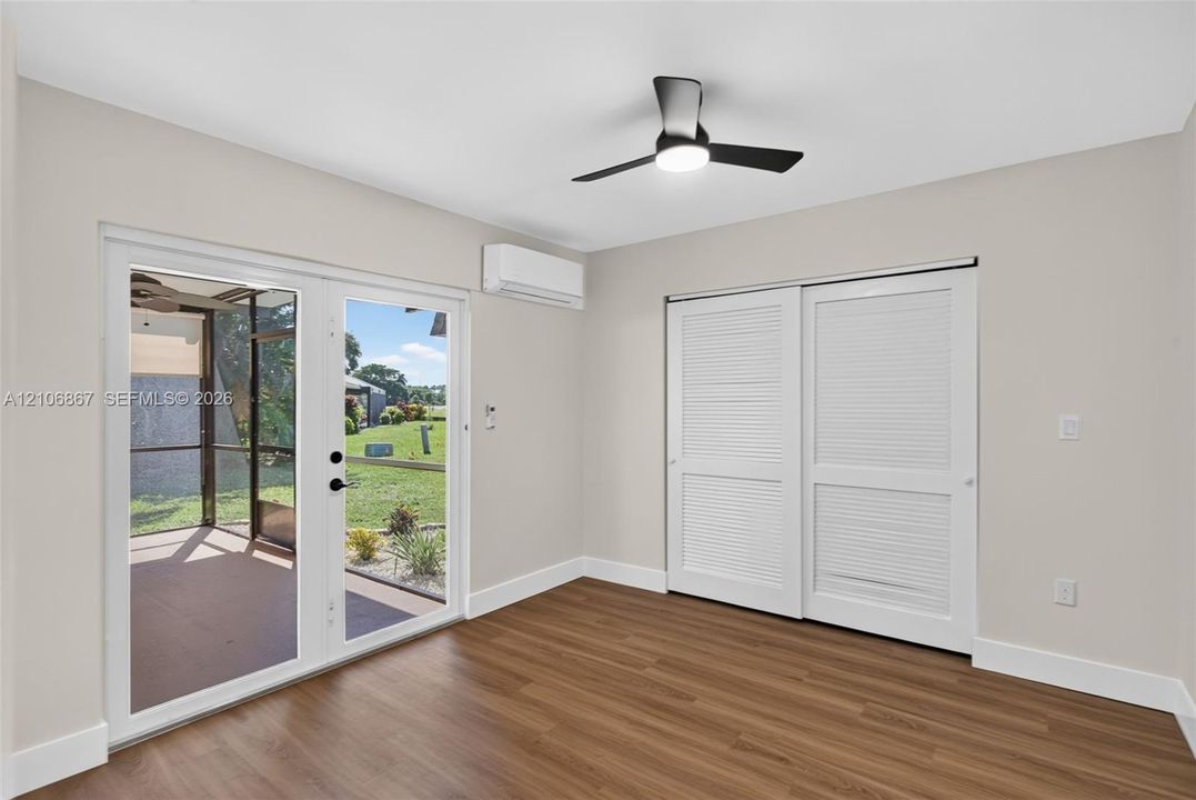 Room featuring wood-finish flooring, dual French doors, a wall-mounted ductless air conditioning unit, louvered-panel closet doors, and a ceiling fan with integrated lighting