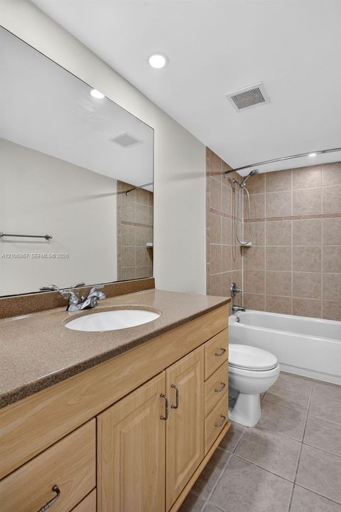 Bathroom featuring a wood-finish vanity with a stone-composite countertop, full-width mirror, tile flooring, and a tub-shower combination with tiled surround