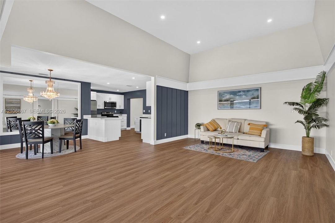 Vaulted ceilings, wood-finish flooring, vertical panel wainscoting, recessed lighting, and kitchen cabinetry featuring a quartz-topped peninsula