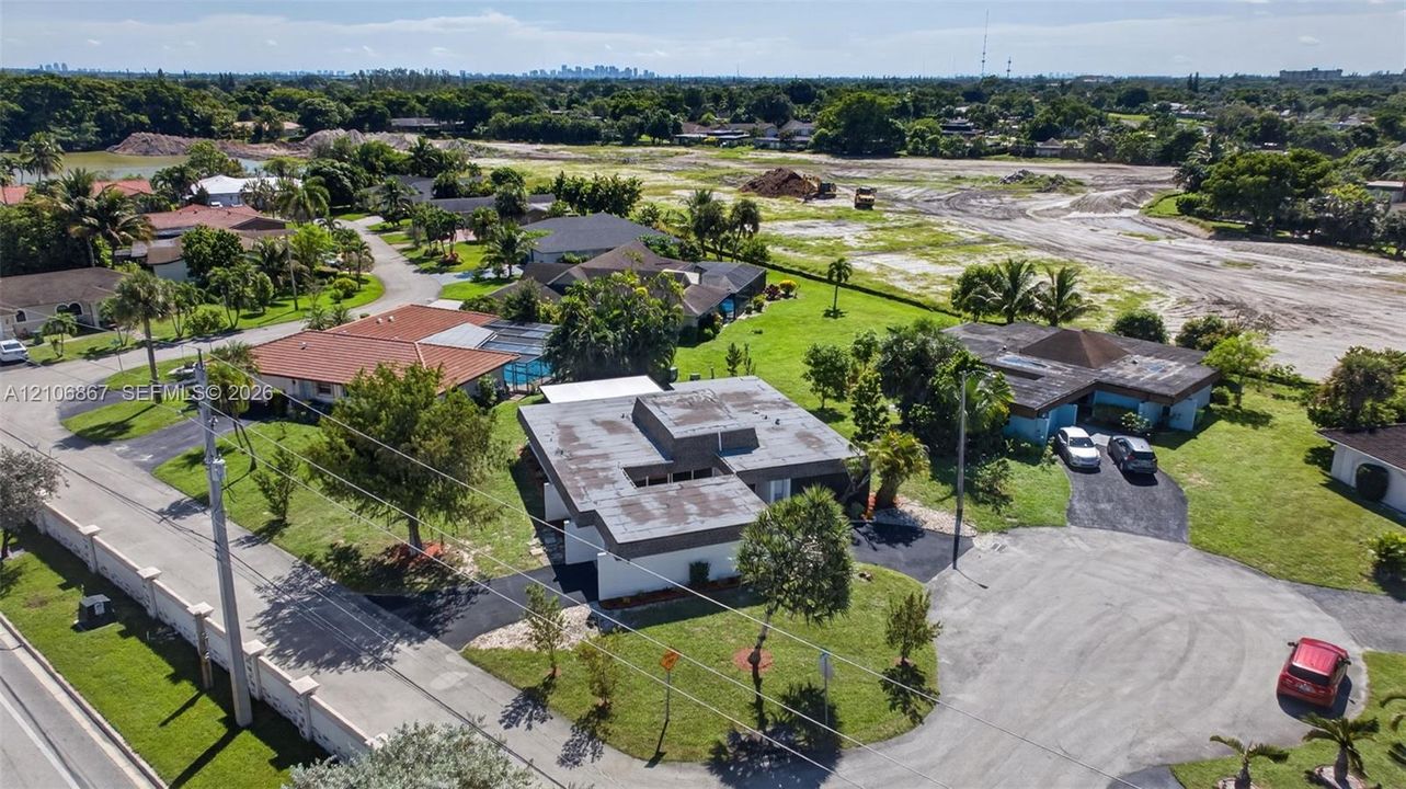 Aerial perspective featuring a flat-roof residence, asphalt driveway, and surrounding lawn area with mature landscaping