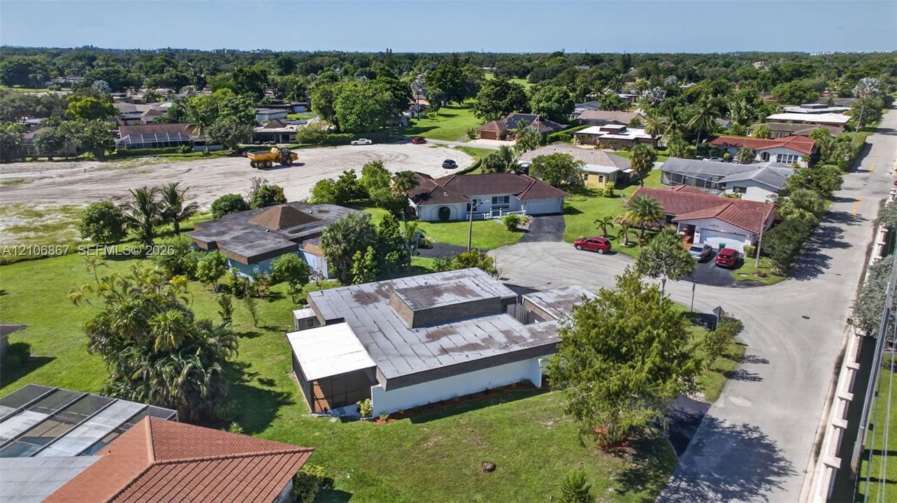 Aerial perspective of a low-profile residential property featuring a flat roofline, an attached screen-enclosed patio, concrete driveway, and mature landscaping within a suburban setting
