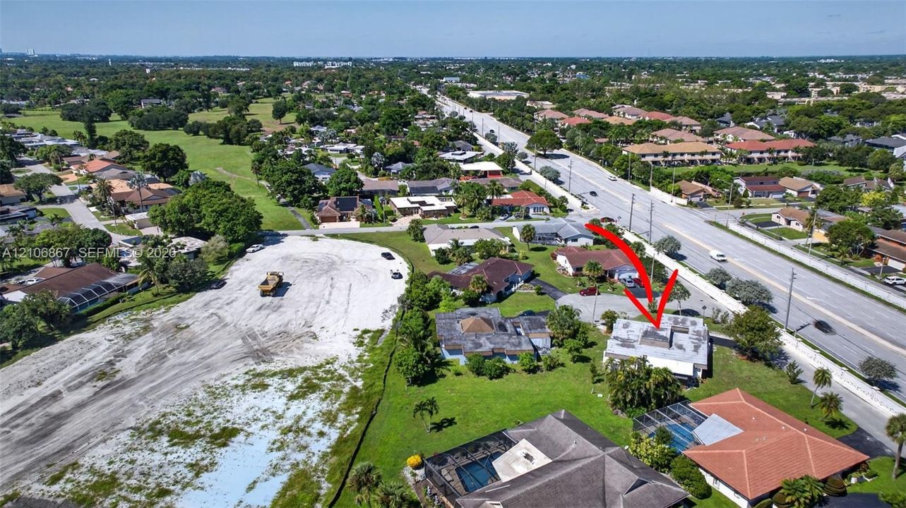 Aerial perspective of residential lot featuring a flat-roofed structure, paved driveway, and established greenery