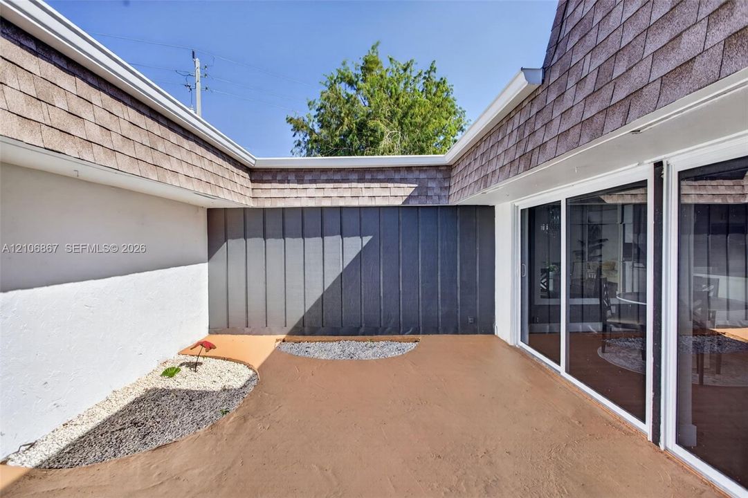 Enclosed courtyard featuring smooth-finish concrete flooring, vertical metal panel siding, a shingle roofline, and glass sliding doors