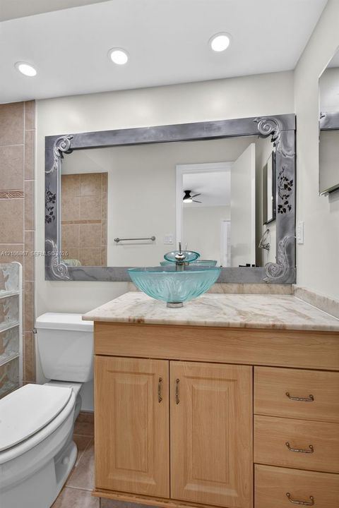 Bathroom vanity featuring a natural stone countertop, glass vessel sink, light wood cabinetry, and a decorative framed mirror