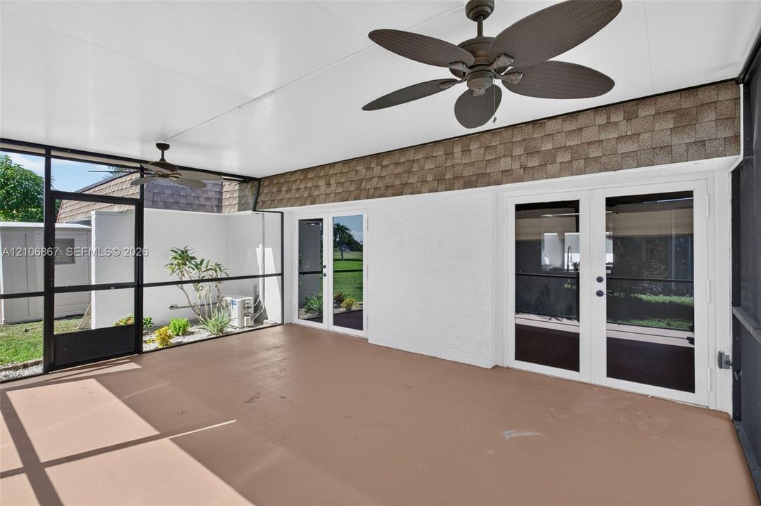 Screened-in lanai featuring dual ceiling fans, solid surface flooring, and double glass-paned doors