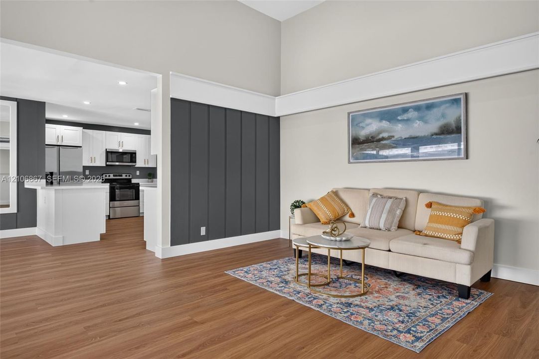 Vaulted ceilings, wood-finish flooring, vertical slat wall paneling, and a kitchen featuring white cabinetry and stainless steel appliances