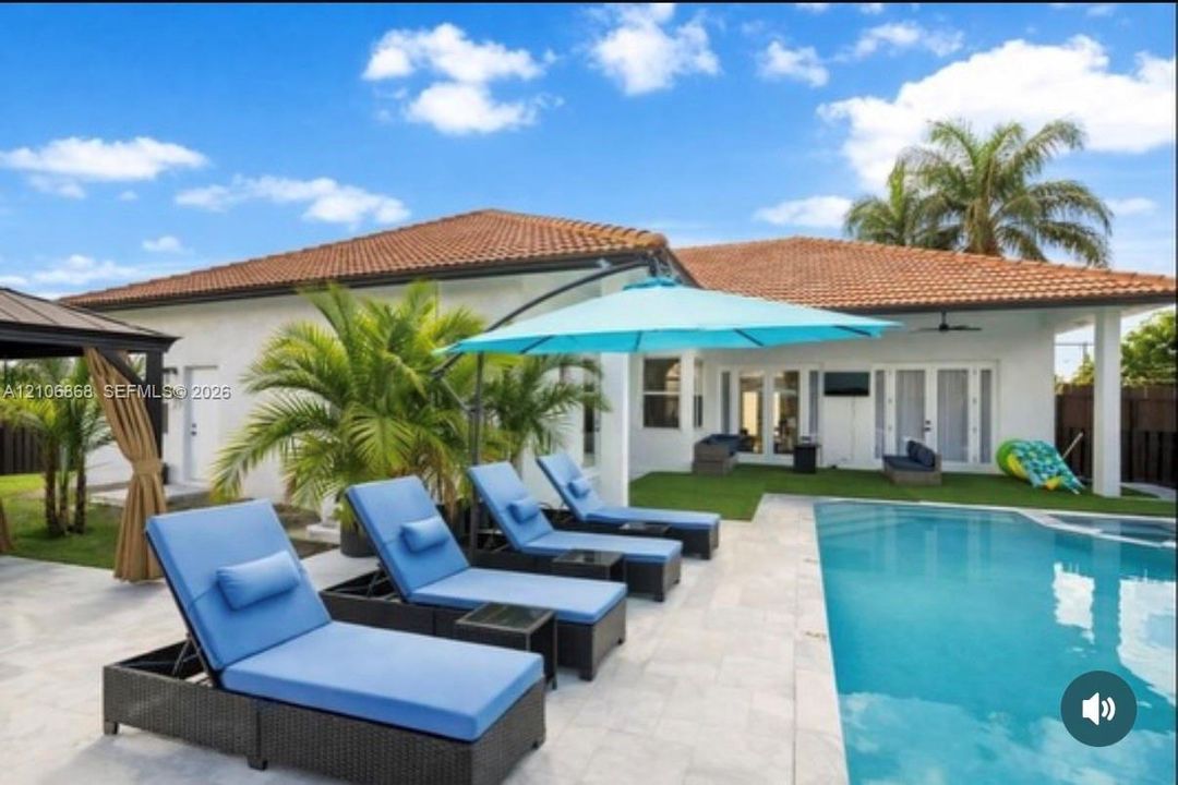 Rear exterior featuring a swimming pool, stone-finish patio, covered porch, and tile roof
