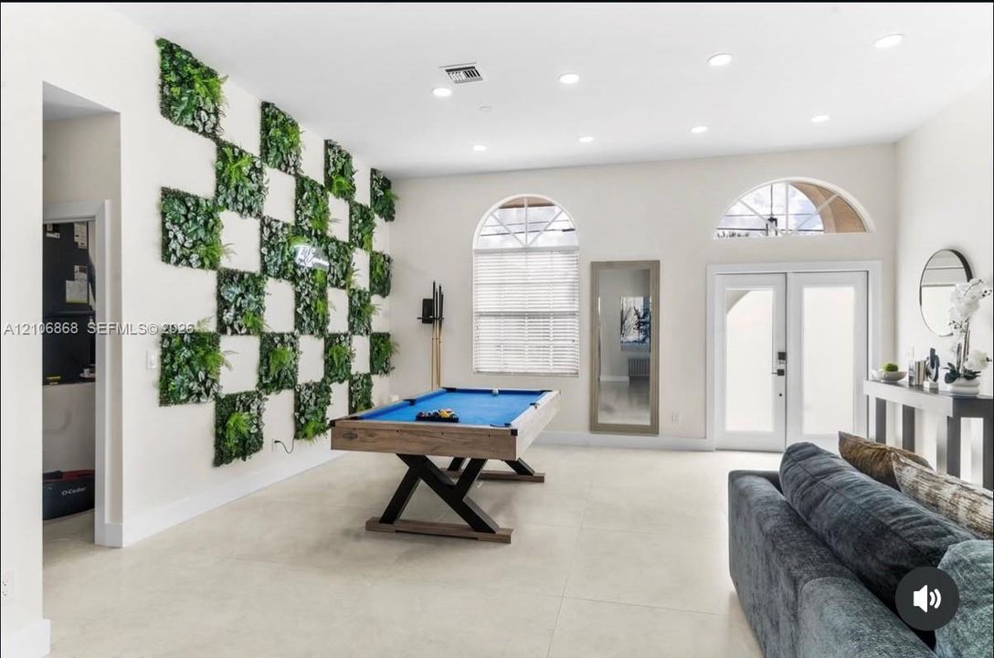 Room featuring large-format tile flooring, recessed ceiling lighting, a decorative green-wall accent, arched windows, and double French-style glass doors