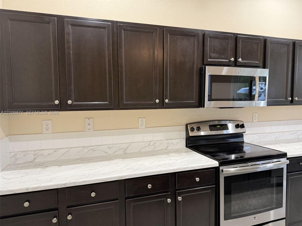 Dark-toned cabinetry featuring shaker-style doors, light-veined countertops, white subway tile backsplash, and stainless steel appliances