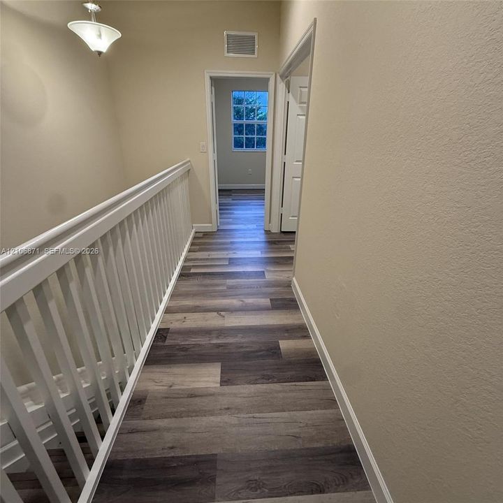 Hallway featuring wood-finish flooring, white spindle railings, and a pendant light fixture