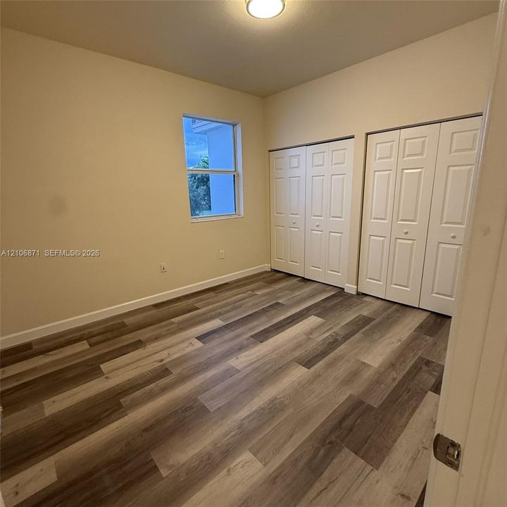 Room featuring wood-finish flooring, dual bi-fold door closets, a single-pane window, and a flush-mount ceiling light fixture