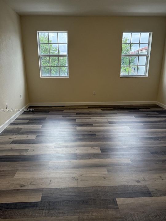 Multi-tone wood-finish flooring, two dual-pane windows with grid detailing, and neutral wall color