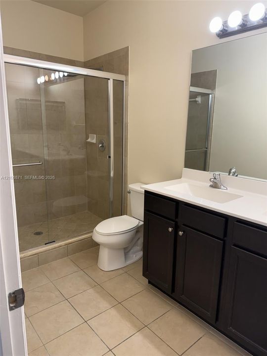 Bathroom featuring a dark wood-finish vanity with a white countertop, an integrated sink, a large wall-mounted mirror, and a walk-in shower with tile surround and a sliding glass door