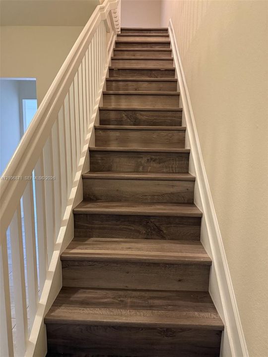 Staircase featuring wood-finish treads and a white painted balustrade with a wooden handrail