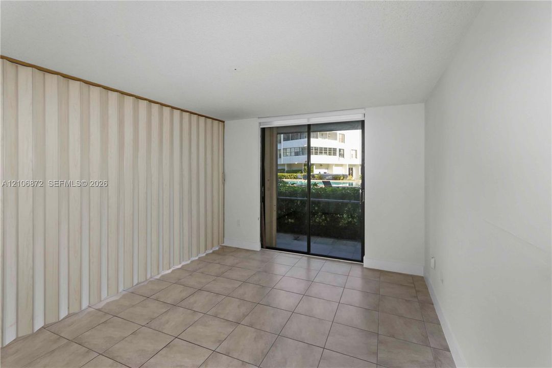 Room with neutral ceramic tile flooring, floor-to-ceiling accordion partition wall, and sliding glass door