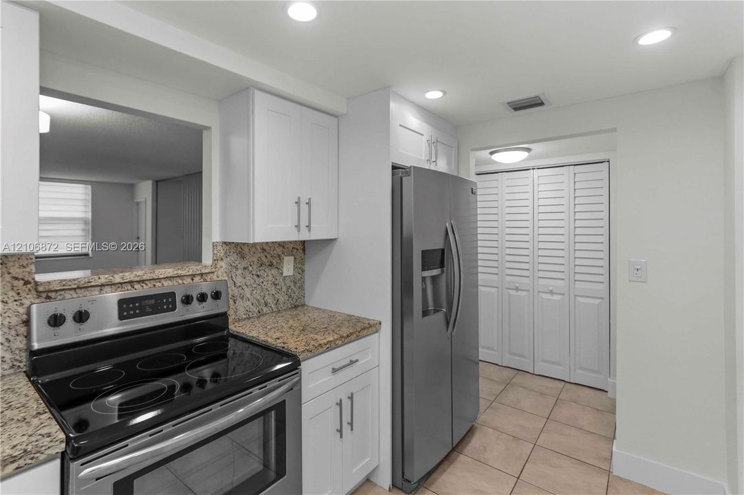 Kitchen featuring white shaker-style cabinetry, stone-finish countertops, stainless steel appliances, recessed ceiling lighting, and tile flooring
