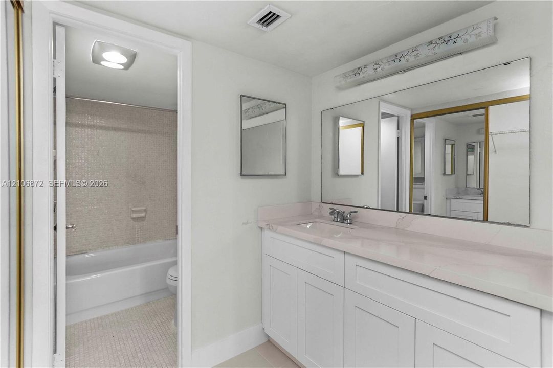 Bathroom featuring a vanity with white cabinetry and a stone-finish countertop, a large wall-mounted mirror, and a tile-surround bathtub