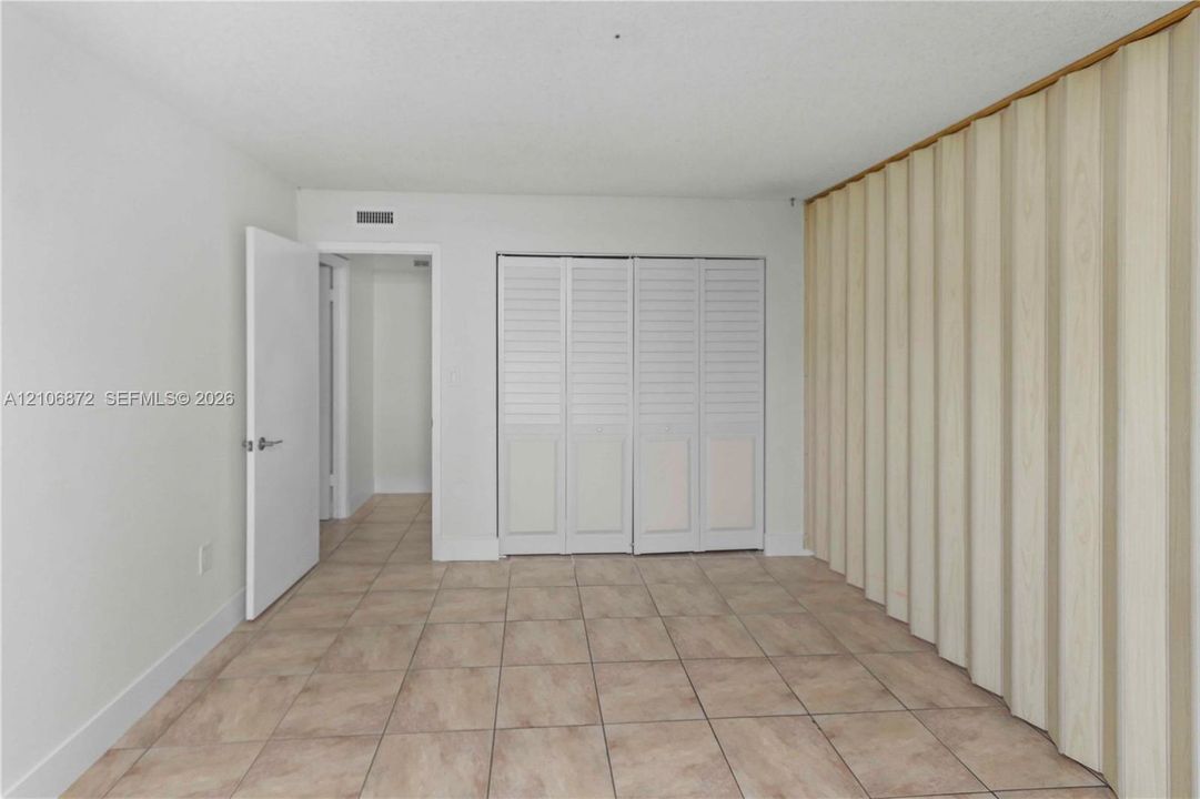 Room featuring ceramic tile flooring, built-in louvered-panel closet doors, and a wood-finish accordion partition wall