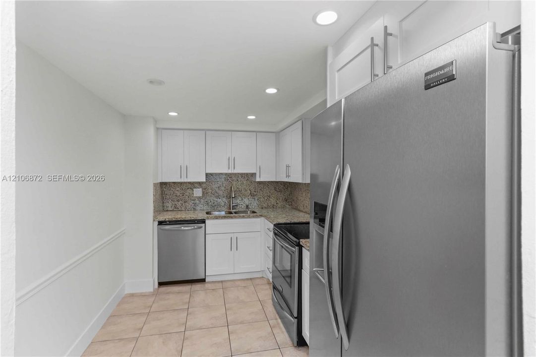 Kitchen featuring white cabinetry, stone-surface countertops, stainless steel appliances, and tile flooring