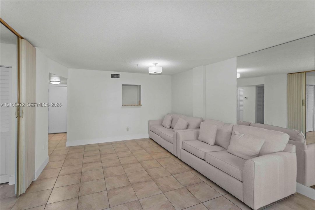 Neutral-toned tile flooring, floor-to-ceiling wall-mounted mirror, inset wall niche, and flush-mount lighting fixtures