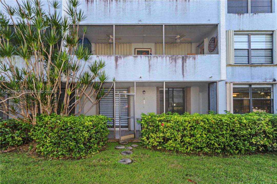 Ground-level screened patio featuring built-in ceiling fans, manicured perimeter shrubbery, stepping-stone pathway, and sliding glass entry