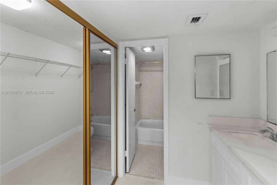 Full-length mirrored closet doors, solid-surface vanity countertop, undermount sink with chrome-finish faucet, recessed lighting, and tiled shower enclosure