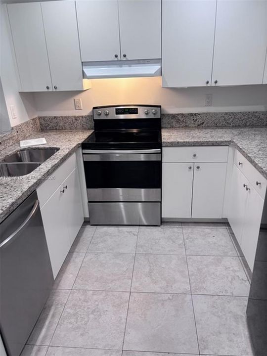 Kitchen featuring white cabinetry, stone-surface countertops, stainless steel appliances, a double-basin undermount sink, and tiled flooring