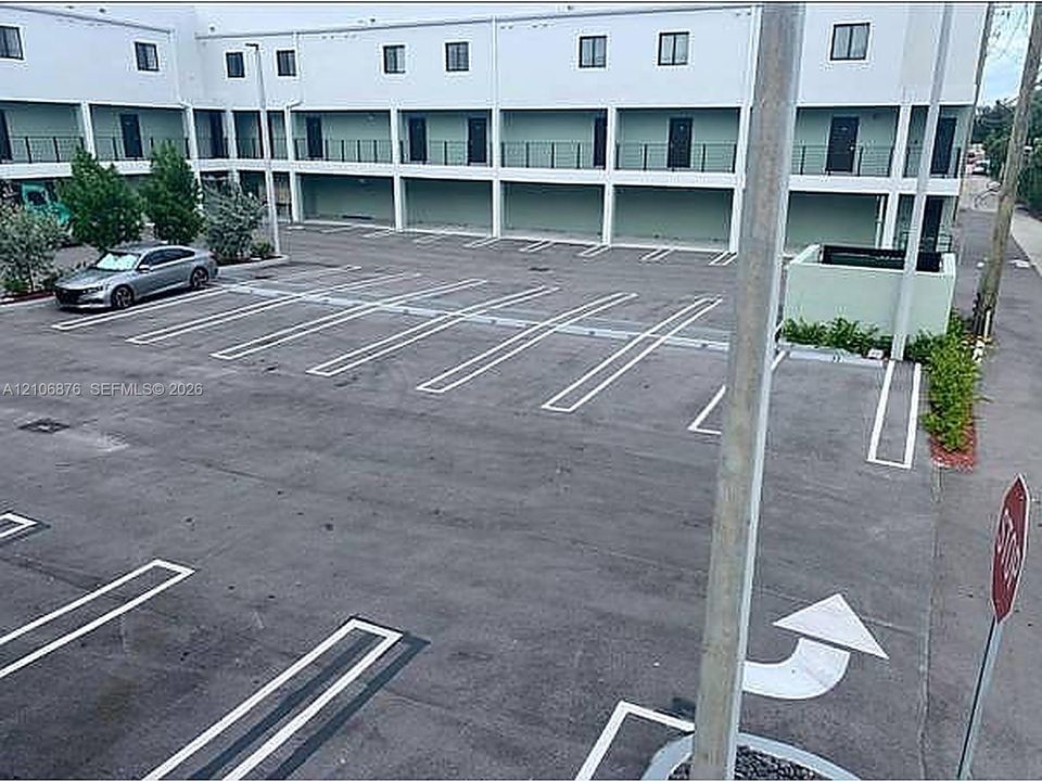 Asphalt parking area with painted stalls, multi-level building exterior with individual entry doors, and metal railings