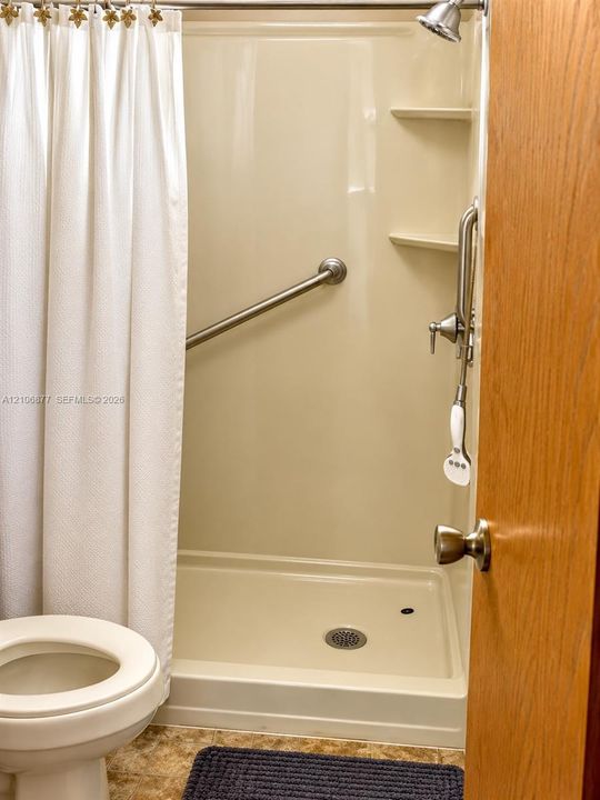 Shower stall with integrated shelving, handheld shower fixture, and wall-mounted metal grab bar