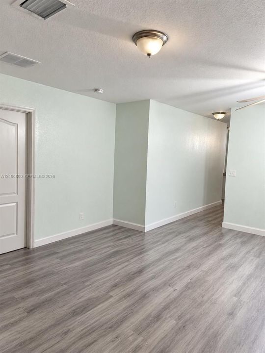 Wood-finish flooring, neutral wall tones, multi-panel interior door, and flush-mount ceiling light fixtures.