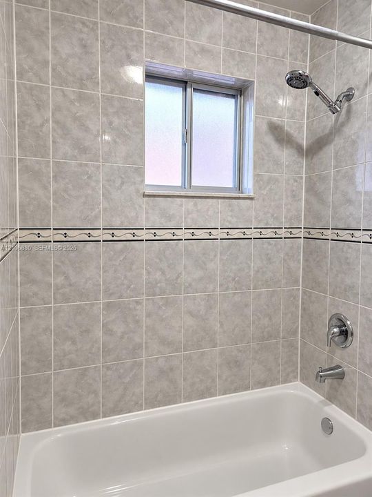 Shower and tub combination featuring full-height neutral ceramic tile surround, decorative accent tile border, chrome showerhead, and sliding window.