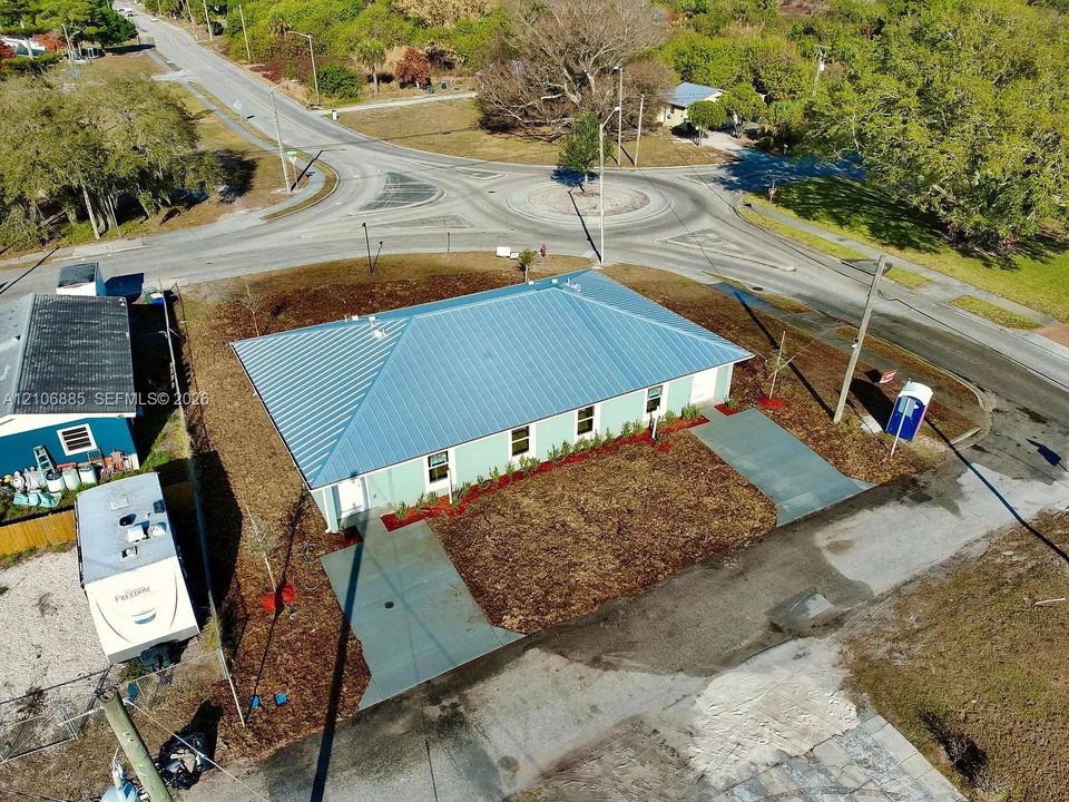 Corner lot property featuring a light green exterior, a standing-seam metal roof, and concrete driveway access