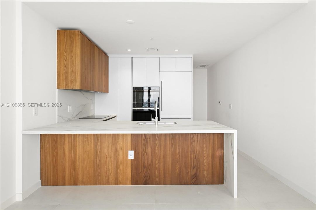 Kitchen featuring a center island with a stone-finish countertop and waterfall edge, two-tone wood-finish and flat-panel cabinetry, built-in wall oven, and integrated refrigerator