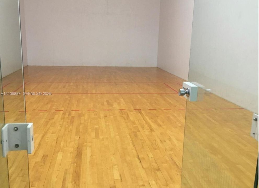 Recreational court featuring wood-finish flooring, glass panel entryway, and high-clearance walls with court boundary markings
