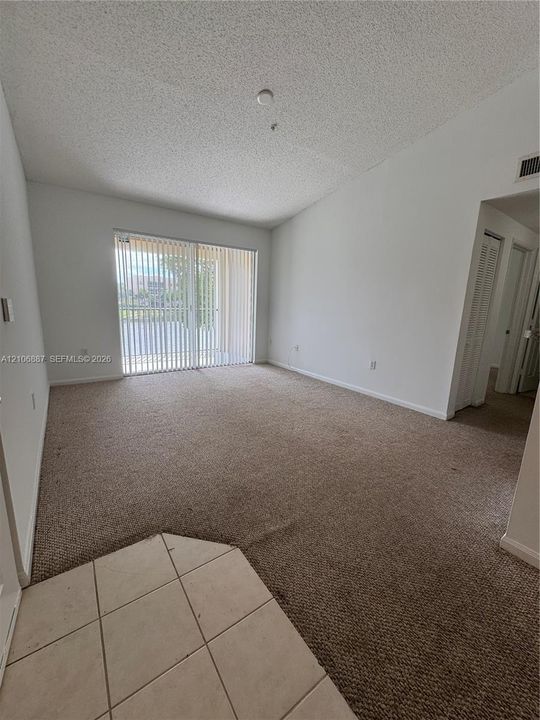 Living area featuring vaulted ceilings, neutral carpeting, sliding glass doors, and tiled flooring at the entry