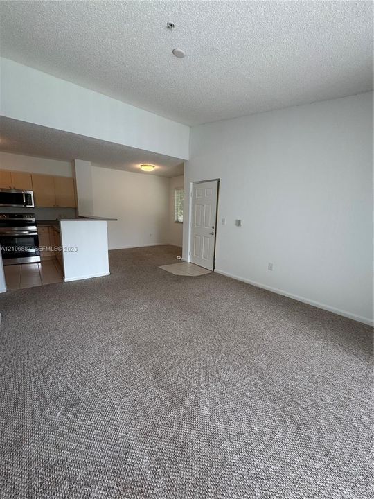 Open-concept interior featuring high vaulted ceilings, carpeted flooring, and a kitchen peninsula with integrated stainless steel appliances