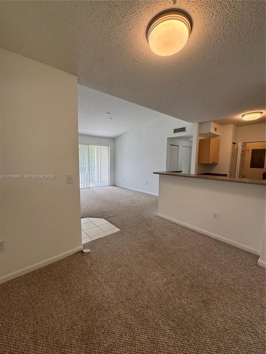 Interior space featuring neutral carpeting, a kitchen breakfast bar with countertop, tile entryway flooring, and sliding glass doors