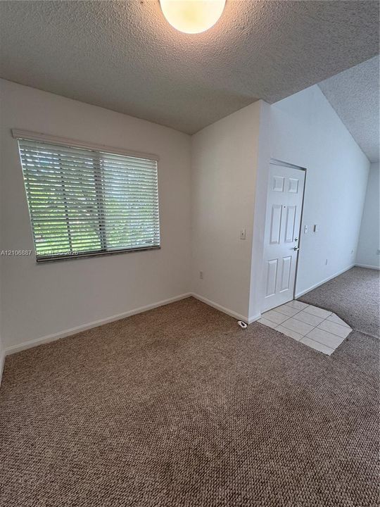 Interior area featuring vaulted ceilings, textured wall finishes, neutral carpeting, a tiled entryway, and horizontal window blinds