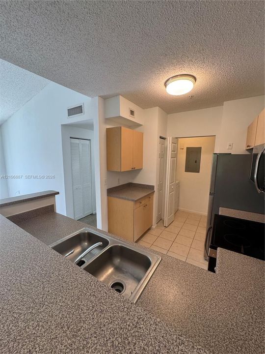 Kitchen featuring a dual-basin stainless steel sink, solid-surface countertops, light wood-finish cabinetry, and ceramic tile flooring