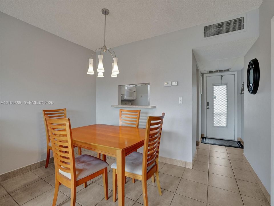 Ceramic tile flooring, pass-through opening to kitchen, multi-light metal pendant fixture, and entry door with glass insert