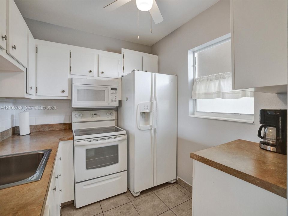 Kitchen featuring white cabinetry, solid-surface countertops, tile flooring, an over-the-range microwave, and a white appliance suite