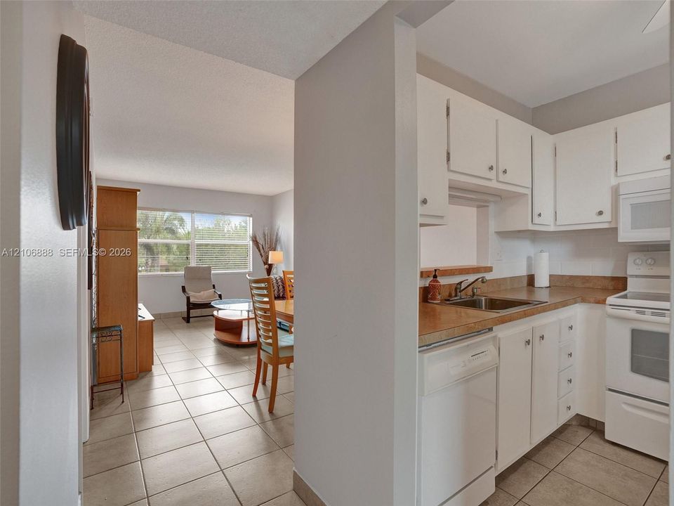 Kitchen featuring white cabinetry, neutral-toned countertops, tile flooring, and integrated white appliances
