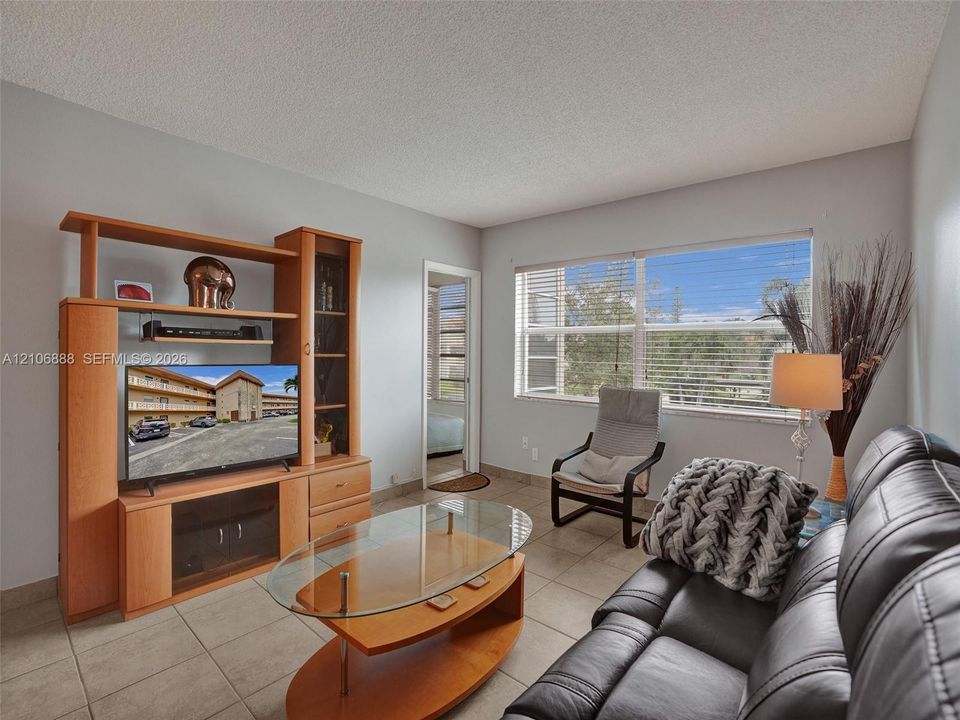 Living area featuring large format ceramic tile flooring and a wide window with horizontal blinds