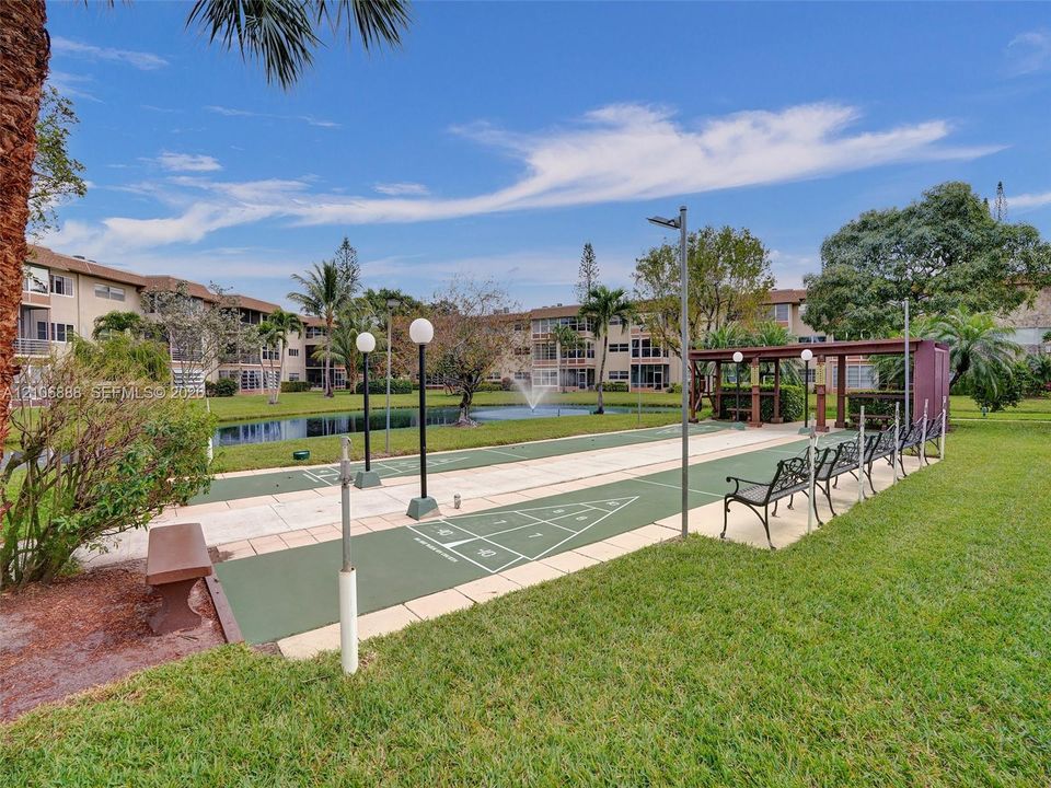 Outdoor recreation area featuring a shuffleboard court, pergola, pond with fountain, and manicured green space