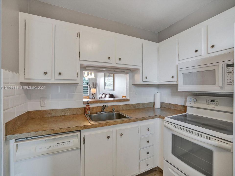 Kitchen featuring white shaker-style cabinetry, white subway tile backsplash, solid-surface countertops, an undermount stainless steel sink, and built-in appliances
